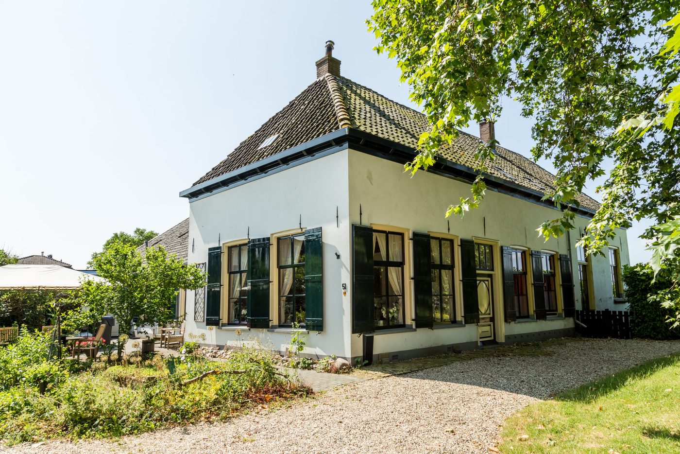 Karakteristieke witte boerderij met donkergroene luiken en gele kozijnen