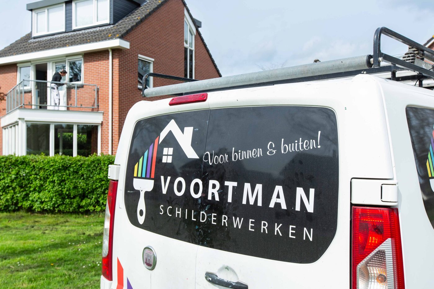 De bus van Voortman Schilderwerken bij een woning, schilder aan het werk op het balkon